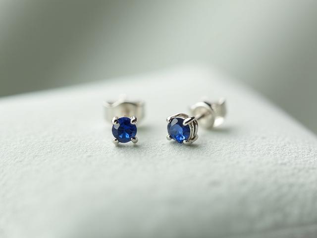 Dainty silver stud earrings with a small birthstone, on a velvet cushion.